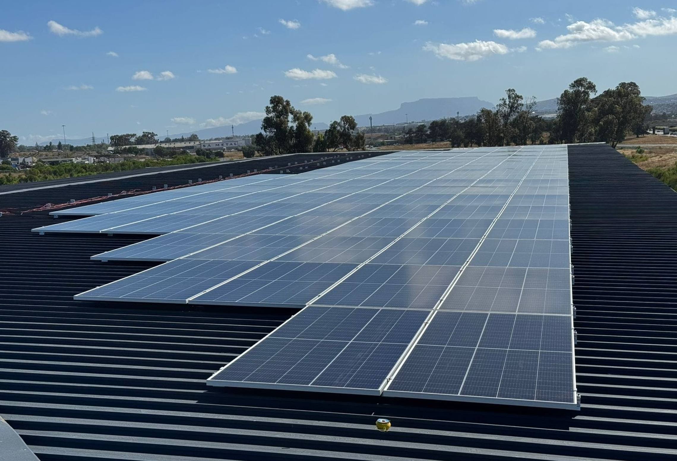 Large commercial solar panel array installed on a dark corrugated IBR metal warehouse roof in Cape Town, South Africa.